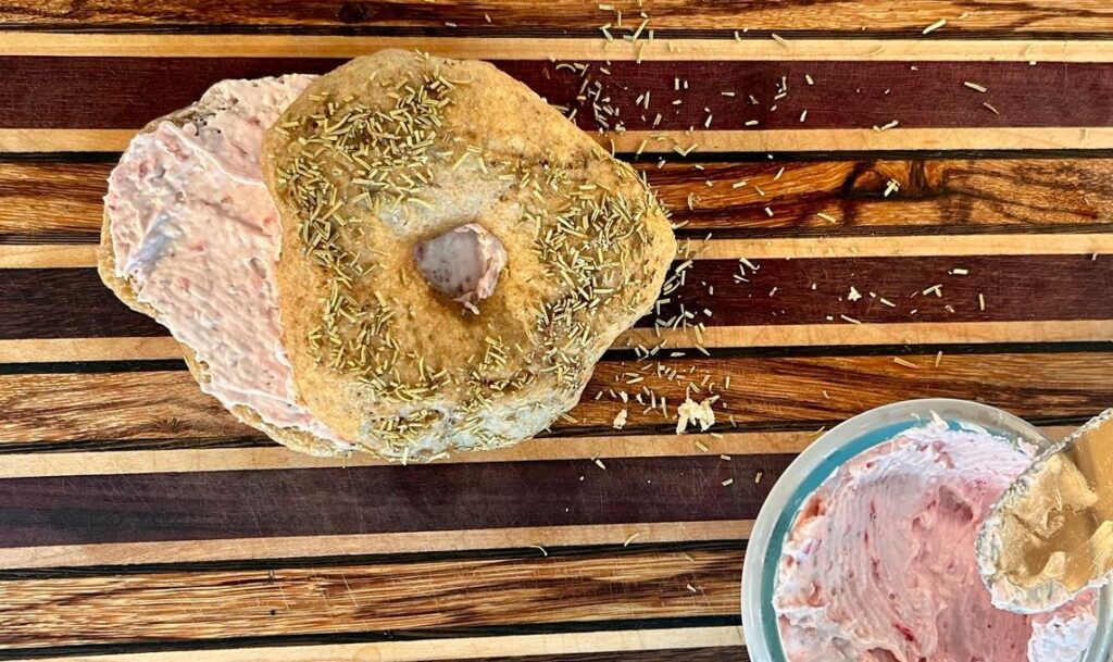 Image of a sourdough bagel with rosemary topping and stawberry cream cheese. dough page.