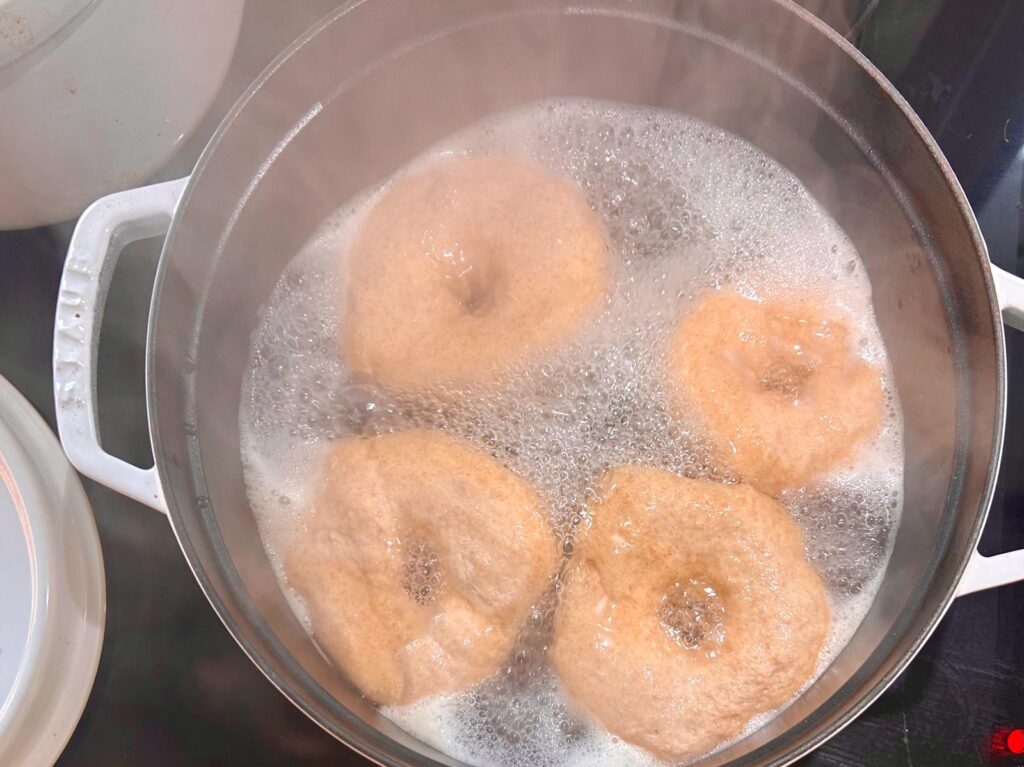 Four bagels boiling in a pot for a minute and thrity secends on each side. 