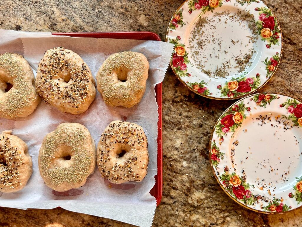 Bagles that have just been boiled are dipped into a plate of seasoning to coat the top of the bagel for flavor.