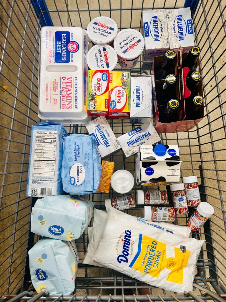 Shopping cart full of ingredients to make a cofetti flavored wedding cake. the shoping cart also has a 6 pack of ocean lab beer.