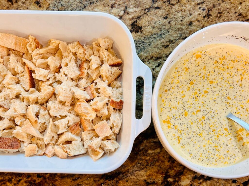 Torn bread lining the bottom of a casserole dish next to a bowl of egg mixture that will be poured over the bread.