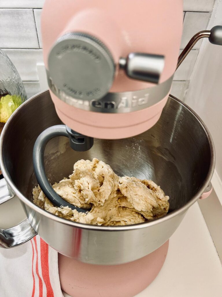 This images features sourdough tortilla dough being kneaded by a kitchen aid mixer with a dough hook.