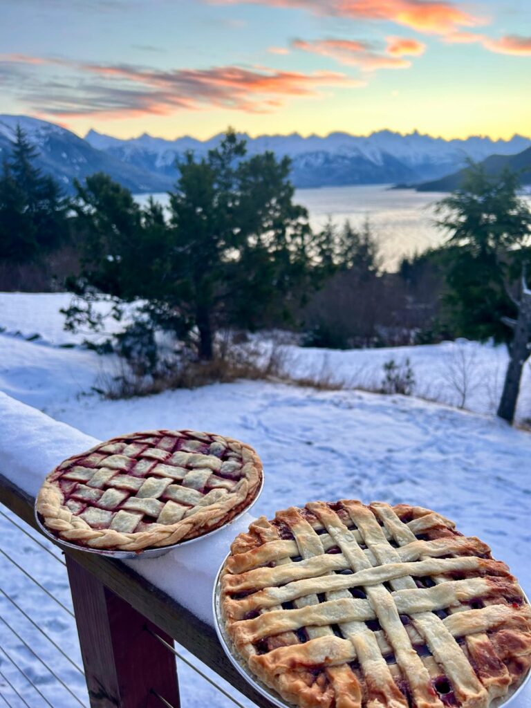 Two pies cooling on a railing covered in snow with a view of Haines, Alsaka.